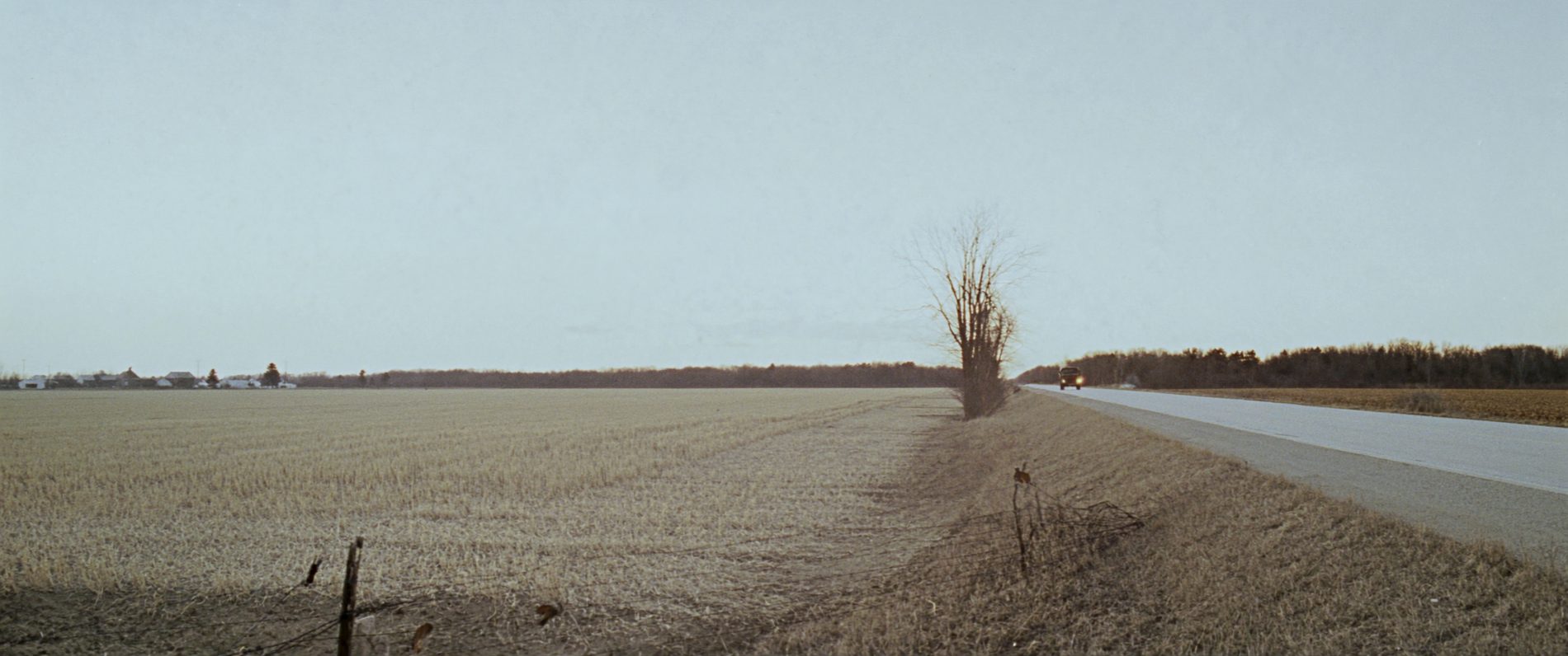 A two-lane highway running between winter fields in northwest Missouri at dusk, with a line of bare trees on the horizon.
